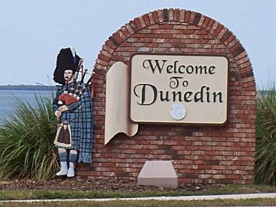The Welcome To Dunedin monument sign on the causeway, with its brick arch and Scottish bagpiper figure, the water behind it
